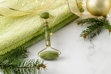 Jade facial roller for anti-aging skin massage, fir tree branch, a soft towel on marble table.