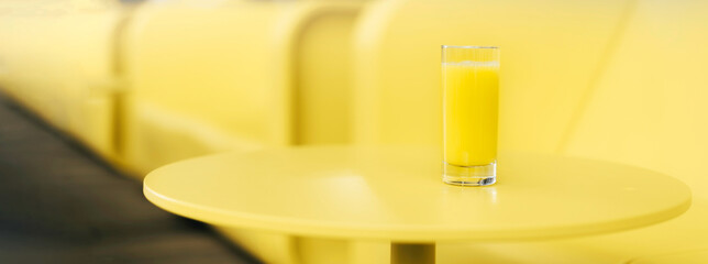 Bright yellow sofa, table, glass of juice. Minimalistic style outdoor interior. Demonstrating trendy Color of the Year 2021. Illuminating Yellow, Ultimate Gray. Duotone. Depression treatment. Banner