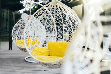 Hanging wicker chair with yellow cushions in minimalistic style outdoor interior. Demonstrating trendy Color of the Year 2021. Illuminating Yellow and Ultimate Gray. Duotone. Depression treatment