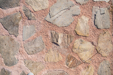 The surface of a pink wall made of concrete and roughly processed beige and gray stones as an abstract background