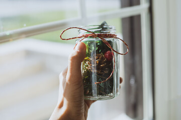 Hand holding Christmas decorations in a jar with ribbon in front of a window