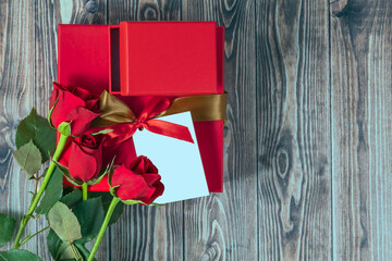 Red roses and gift box with ribbon. Valentine's day, birthday festive background with copy space on wooden backdrop