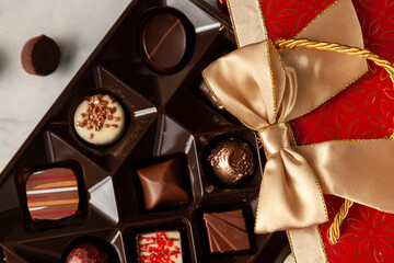 Assorted chocolates in elegant red gift pack with golden ribbon put on top of a white marble background. A stylish christmas and valentines day gift option with tasty pieces of chocolate.