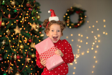 cheerful funny little girl baby with new year gifts by the tree