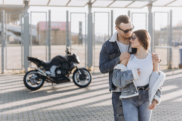 Obraz na płótnie Canvas Sexy girl and guy hugging and kissing on the background of a sports motorcycle standing in the parking lot near a large football stadium