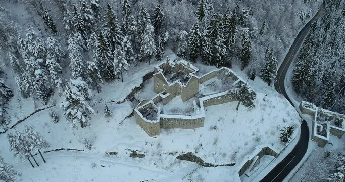 Aerial drone overhead view of medieval Predil fortress in Slovenia. Paved countryside road between forest. Cold winter in Alpine valley. Beautiful landscape covered with snow. Descending