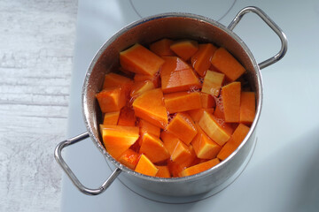 Pieces of red pumpkin are cooked in a saucepan on an induction hob.