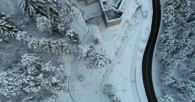 Aerial drone overhead view of medieval Predil fortress in Slovenia. Paved countryside road between forest. Cold winter season in Alpine valley. Beautiful landscape covered with snow. Forward, ascend