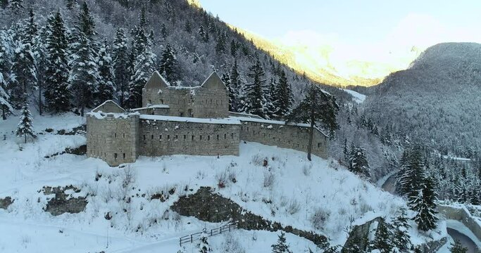 Aerial drone view of Predil fortress in Slovenia. Cold winter season in Alpine valley. Alps mountains in background. Beautiful landscape covered with snow. Dynamic moving