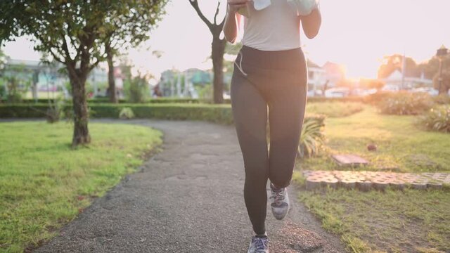 Young active woman wear sport clothes running inside the park, beautiful morning sunlight on background, cardio exercise, listening to music while jogging alone, positive energy, fit and strong body