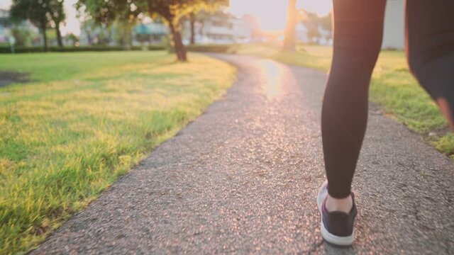 Low angle shot rear view of young sporty woman run inside the park on the running path way, beautiful orange sunset horizon light, cardio exercise, begining of new ssport resolution positive energy