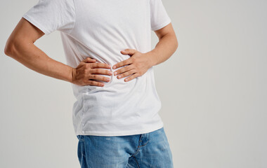 guy in a t-shirt and jeans touches his hands near the abdomen pain stomach problems appendicitis