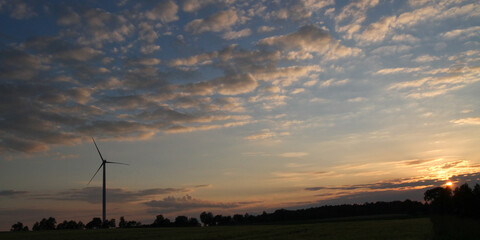 Silhouette of a sngle wind turbine on the horizon with colorful sky in the background at sunset