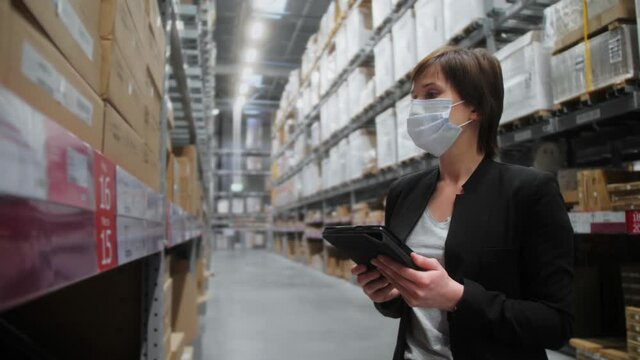 Warehouse supervisor wearing protective face mask check goods stock in warehouse by digital gadget. Concept of e-commerce.