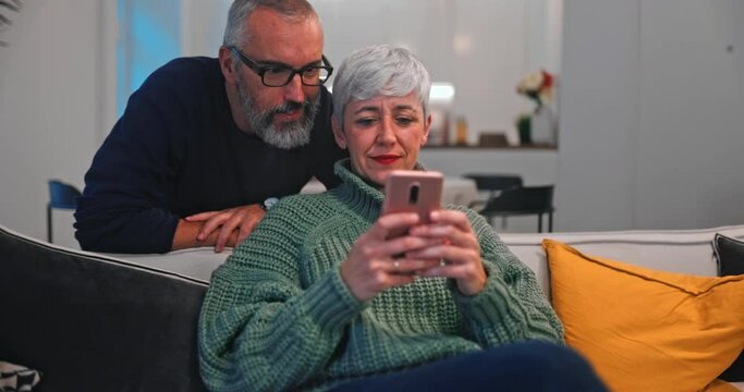 Senior woman showing smartphone to husband while sitting on sofa