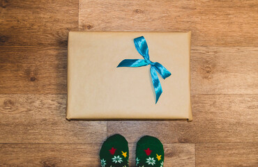 A flat lay image of a wrapped gift with a blue ribbon and Christmas socks with a wooden flooк in the background 