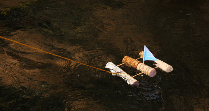 A homemade toy sailing raft made from wine corks and toothpicks floats on a bubbling brook