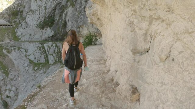 Cain, Spain - September 1, 2020: Female hiking trough the Cares Route in the heart of Picos de Europa National Park, Spain. Narrow and impressive canyon between cliffs, bridges and caves