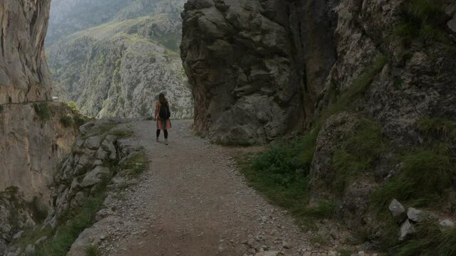 Cain, Spain - September 1, 2020: SLOW MOTION - Female hiking trough the Cares Route in the heart of Picos de Europa National Park, Spain. Narrow and impressive canyon between cliffs, bridges and caves