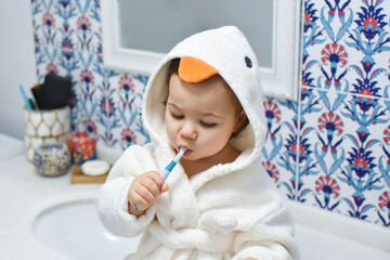 Portrait of cute adorable baby girl or boy brushing teeth in bathroom with bright and white background. Beautiful child and morning dental hygiene in bath. Kids toothbrush concept. Healthy lifestyle.