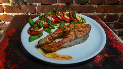 Caprese salad with cherry tomatoes, mozzarella toast and grilled salmon fish on the red brick wall background. Healthy eating concept.