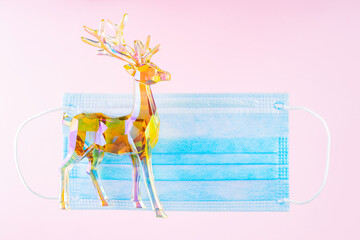 Medical mask and toy deer on a pink background. New year medical concept with holographic deer and protective face mask. Pandemic Christmas concept. Levitation