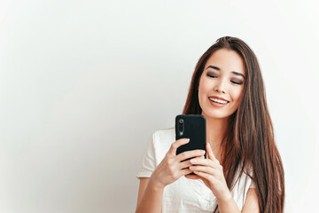 Fototapeta premium Beautiful Asian smiling girl talks on the phone on a white background in a white t-shirt with a beautiful smile