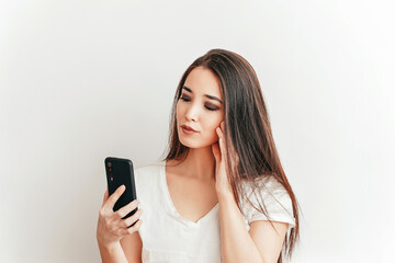 Fototapeta premium Beautiful Asian smiling girl talks on the phone on a white background in a white t-shirt with a beautiful smile
