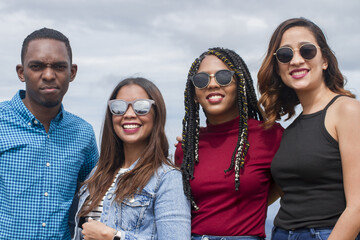 group of four Latin American adventurers friends outdoors smiling and looking to camera using sunglasses half body shot and sky background landscape in dominican republic in a summer day - obrazy, fototapety, plakaty