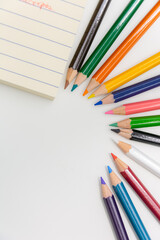Colorful sketch pencils arrranged to form a circle with white background and space for text and a notepad