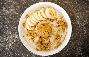 Top view closeup of an oatmeal  with bananas, nuts, and peanut butter on a bowl - Powered by Adobe