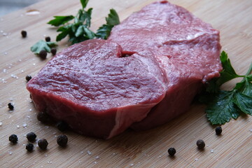 Rump beef steak. The 21 day matured beef meat on the bamboo wooden table with black pepper, sea salt crystals, leaves of parsley. Natural lights.