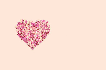 Pink cream sugar is a variety of sprinkles for confectionery. Flat lay in the shape of a heart, on a pastel background.