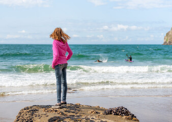 Girl in pink sweatshirt looks out at surfers