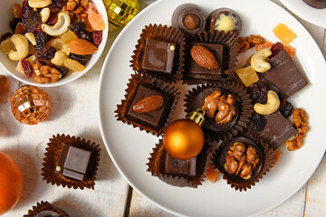 sweet food background for christmas or holiday decoration - chocolate candies, tangerines, nuts and dried fruits on white wood