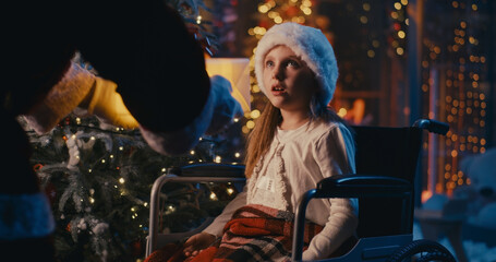 Fototapeta na wymiar Astonished girl on wheelchair receiving present from Santa Claus at night
