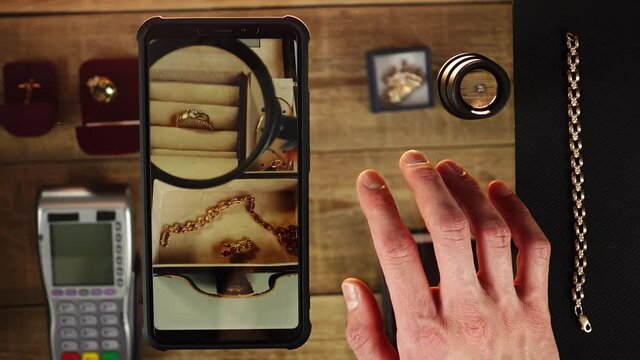 Online evaluating of jewellery on mobile in close-up. Woman shows accessories through loupe to goldsmith by video calling. Man asks to show a ring closer and does thumb up then ok signs. Web pawnshop.