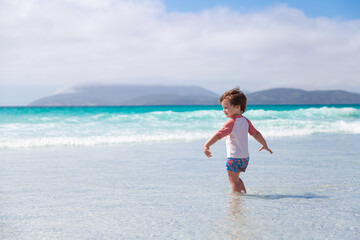 Fototapeta na wymiar Smiling little boy enters to the water sea alone in Cabo Frio beach, Brazil.Caucasian child with the background of beautiful and clear sea.