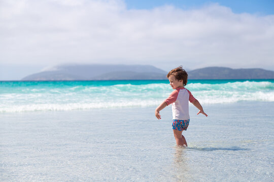 Smiling little boy enters to the water sea alone in Cabo Frio beach, Brazil.Caucasian child with the background of beautiful and clear sea.