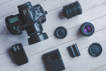 Flat lay with different photoaccessories on white boards: camera, lenses, battery, charger, synchronizer, and lens covers