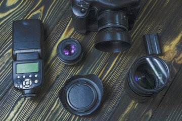Flat lay with different photoaccessories arranged on dark boards: camera, lenses, battery, charger, synchronizer, and lens covers