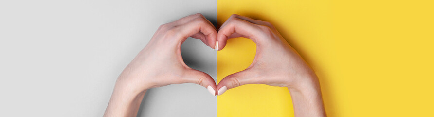 Beautiful female hands with white manicure make a heart on a gray-yellow background. Place for text, copy space, banner format
