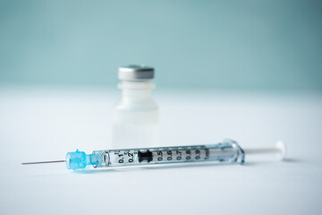 Close up of needle, syringe and vial of vaccine on white table.