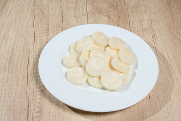 Palm hearts or heart of palm cut into slices on a white plate on a wooden surface. Concept natural food, healthy food.