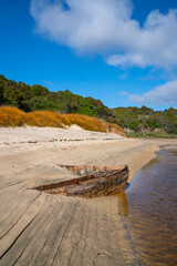 Lines and patterns curving along edge of stream interupted by bow of old wooden boat  stuck in sand