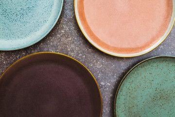 Rustic tableware setting. Multicolored pottery plates used to dress the table. Ceramic handmade dinner collection on a dark gray background. Informal and elegant table setup of dinnerware.