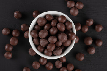 Chocolate balls in white bowl on black background.