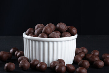 Chocolate balls in white bowl on black background.