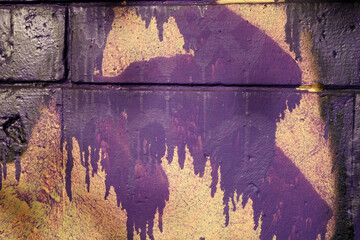 Streaks and splashes of purple paint on an orange porous wall