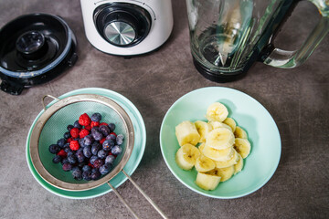 Top down on fresh fruit banana and blueberries and raspberries in bowls on the kitchen counter ready to make fresh smoothie - healthy eating concept